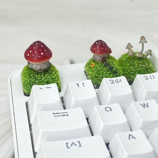 Handcrafted Mushroom Keycap Set  Step into a whimsical world with our Handmade Mushroom Keycap Set, where mushrooms thrive on a bed of lush moss, adding an enchanting touch to your keyboard.  Mystical Details:  Each keycap is a testament to craftsmanship, meticulously created to resemble the beauty of nature. These tiny mushrooms sprout from a bed of moss, making your keyboard a portal to a fairy tale realm.