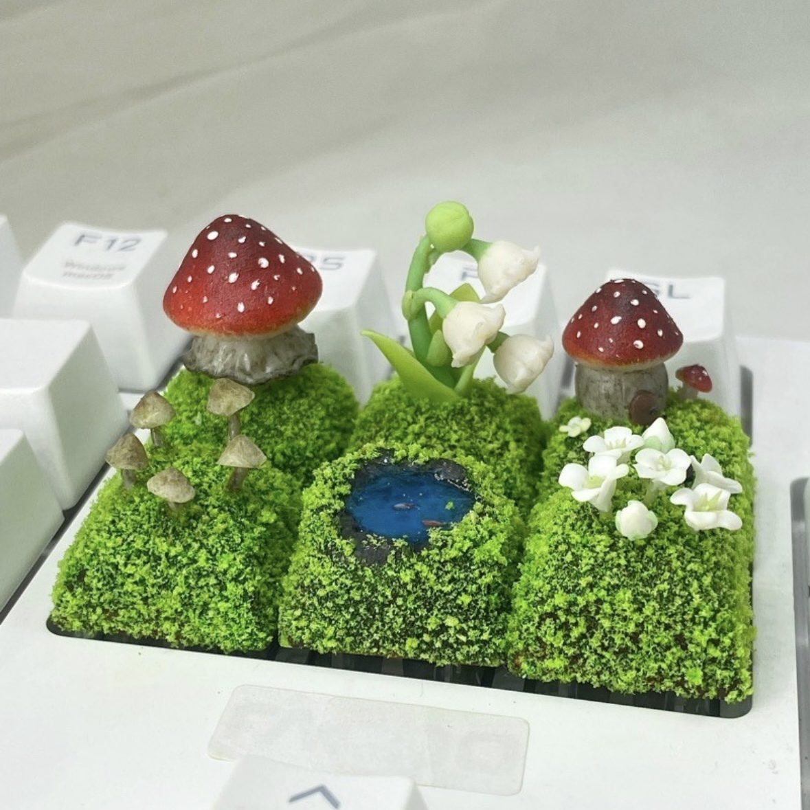 Handcrafted Mushroom Keycap Set  Step into a whimsical world with our Handmade Mushroom Keycap Set, where mushrooms thrive on a bed of lush moss, adding an enchanting touch to your keyboard.  Mystical Details:  Each keycap is a testament to craftsmanship, meticulously created to resemble the beauty of nature. These tiny mushrooms sprout from a bed of moss, making your keyboard a portal to a fairy tale realm.